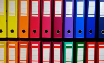 Shelf of multi-colored binders.
