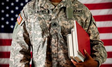 Military student holds books in from of American flag.