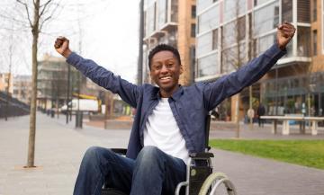 Student in wheelchair celebrates outside university building.